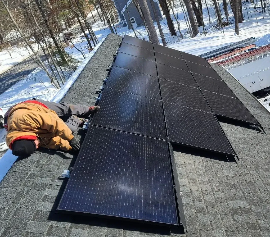 Workers installing black solar panels on a snowy rooftop in winter