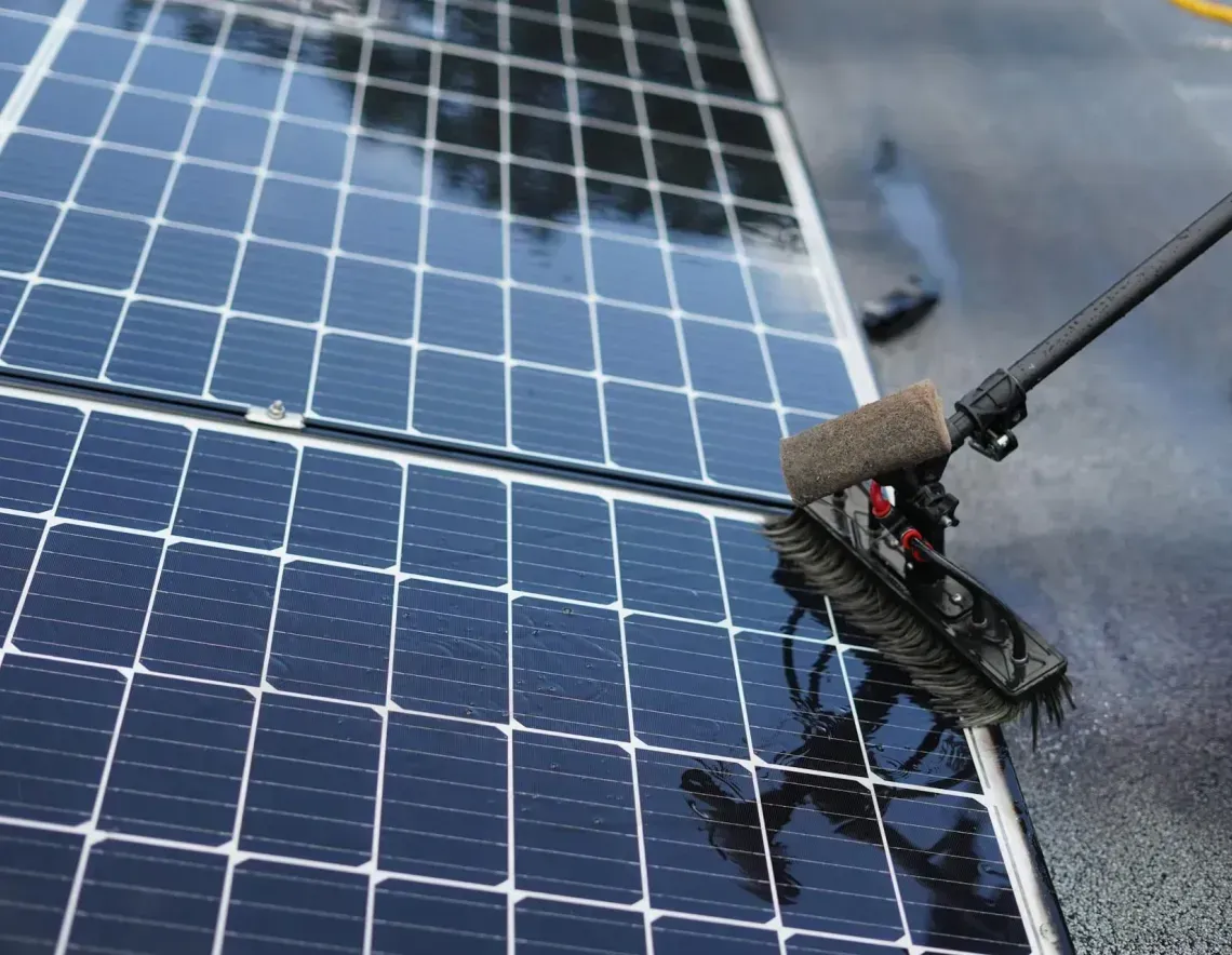Person cleaning solar panels with a brush on a wet rooftop