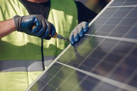 Worker in green vest uses a screwdriver to install a solar panel outdoors.