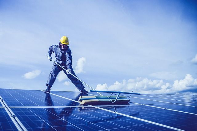 Worker in blue protective suit and yellow hard hat inspecting solar panels under a bright sky
