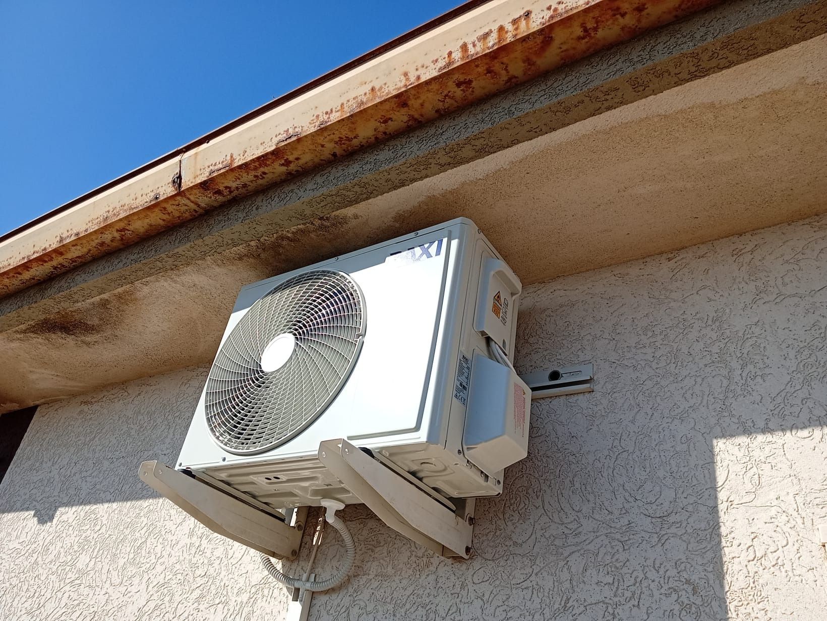 Unità esterna di condizionamento dell'aria montata su una parete in stucco sotto la grondaia del tetto.
