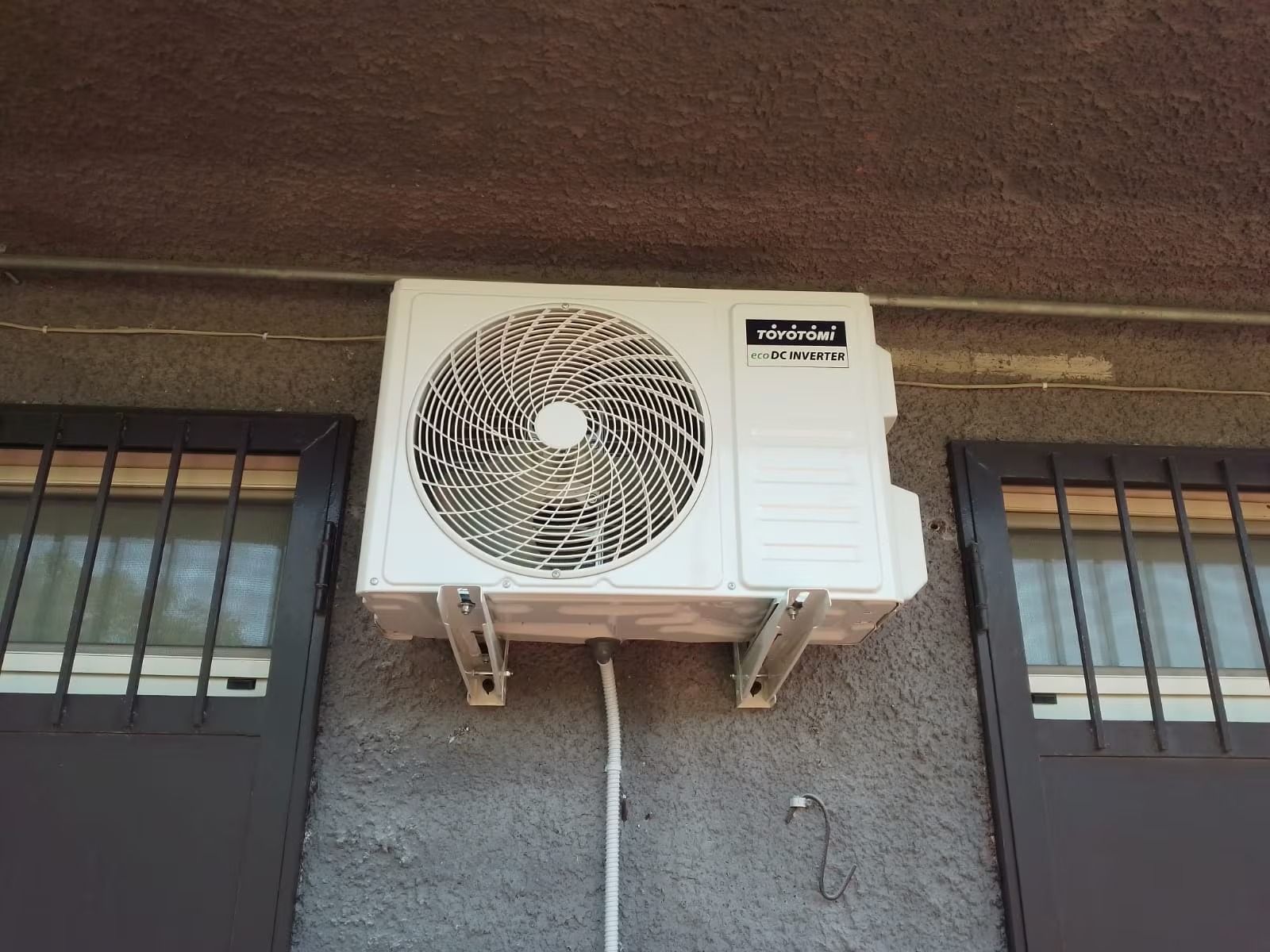 Condizionatore d'aria a parete installato su una parete esterna grigia, sotto una sporgenza del tetto.