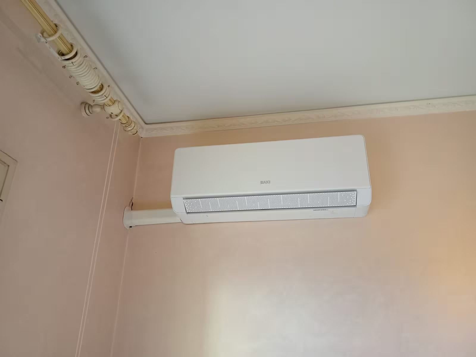 Condizionatore d'aria bianco a parete, installato su una parete rosa pallido vicino al soffitto.