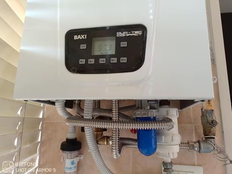Caldaia Baxi a parete con tubi e filtro blu sottostante.