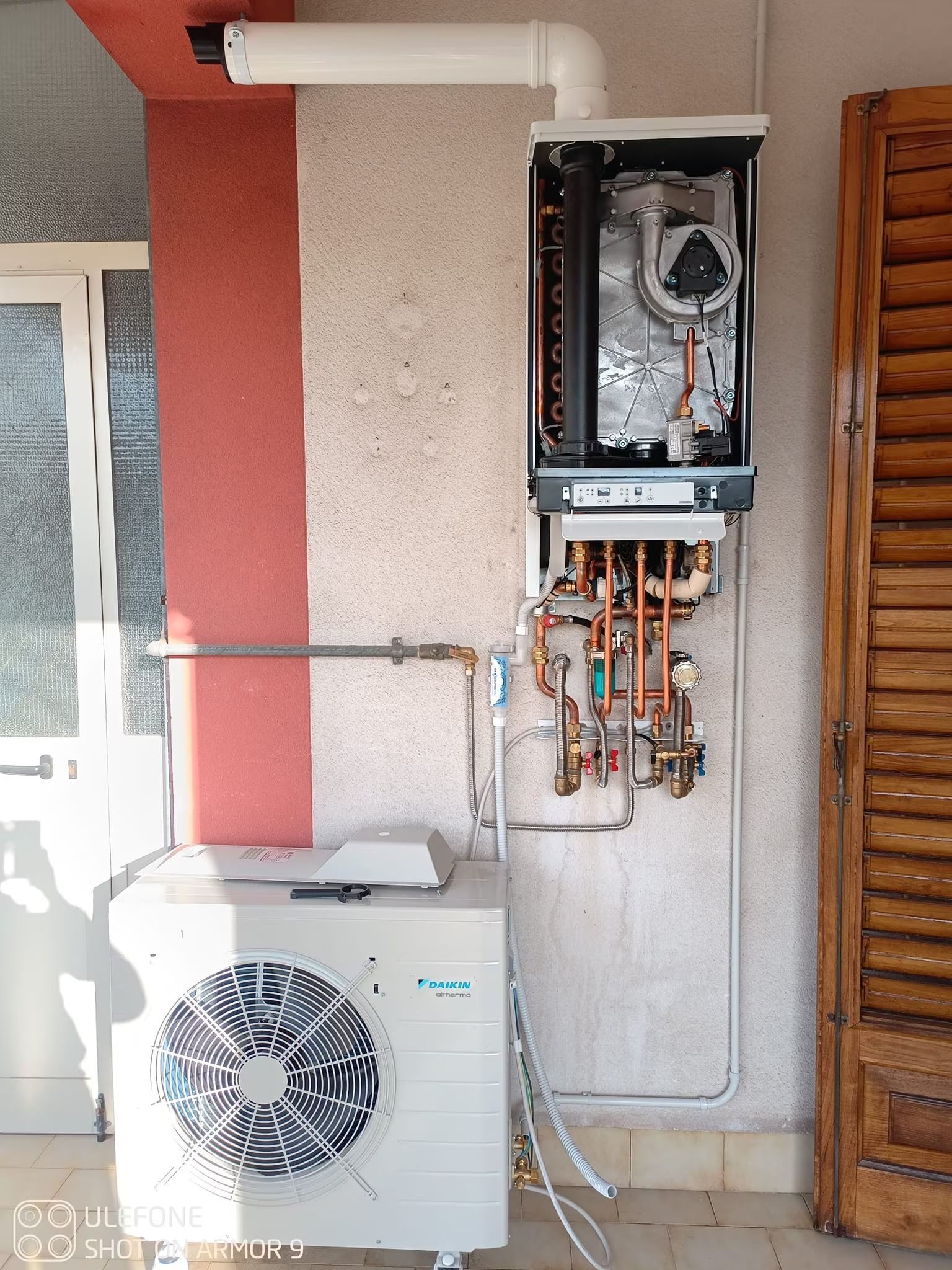 Scaldabagno a gas a parete e unità esterna di climatizzazione accanto a una parete esterna in stucco.