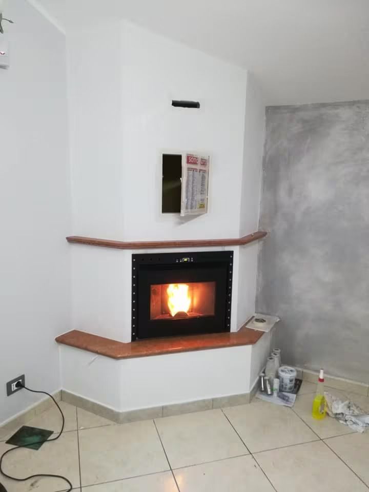 Camino ad angolo in una stanza bianca con fuoco acceso e pavimento piastrellato.