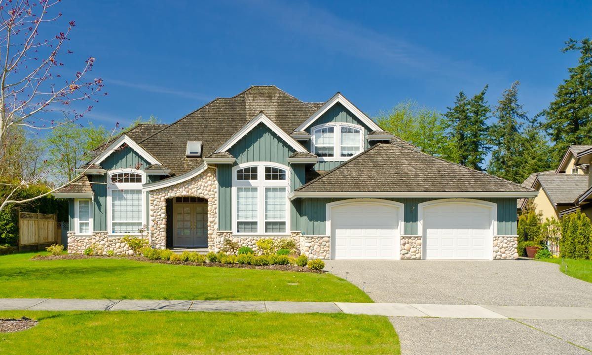 A large house with two garage doors is sitting on top of a lush green lawn. A large house with two garage doors is sitting on top of a lush green lawn.