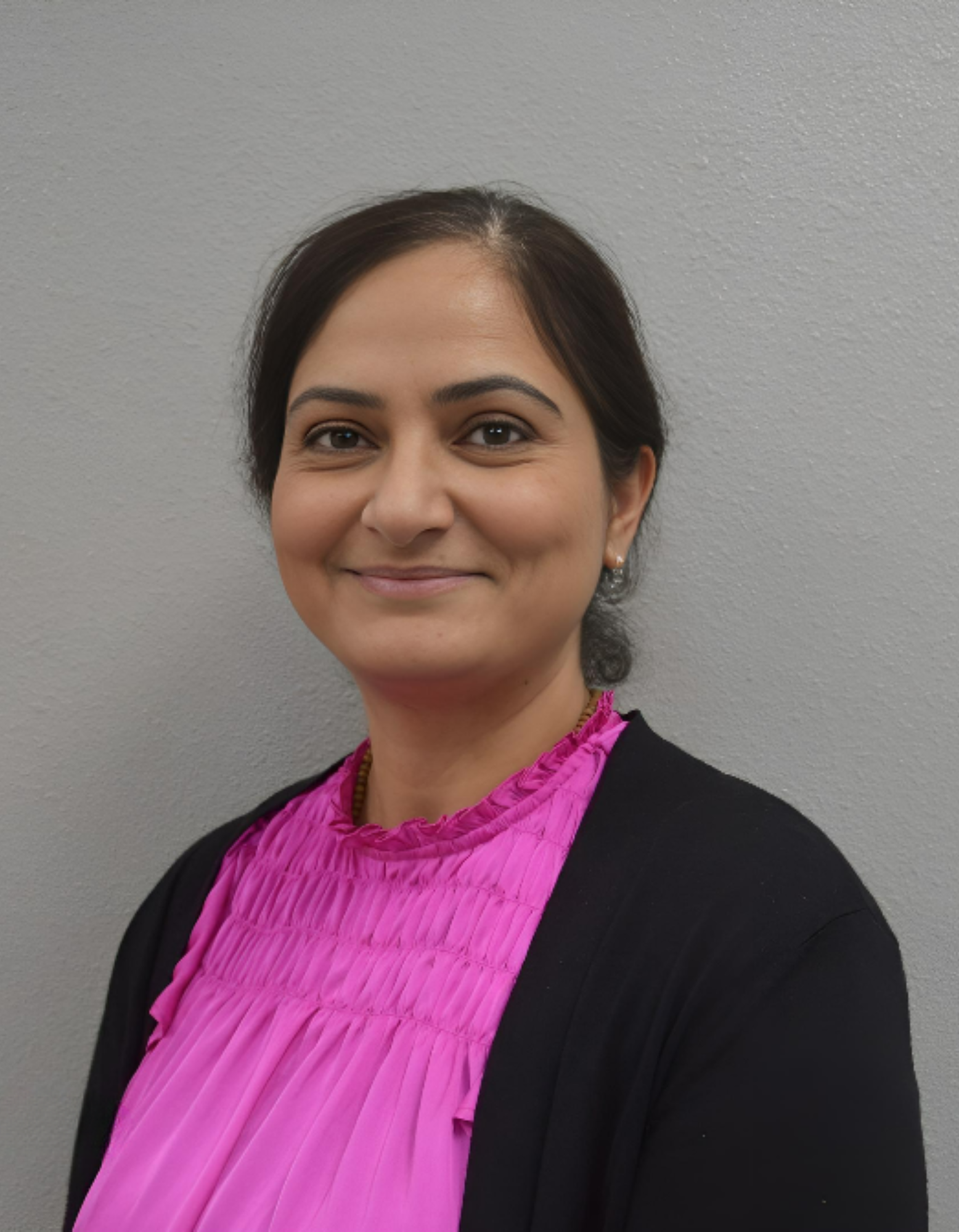 A woman in a pink shirt and black cardigan is smiling for the camera.