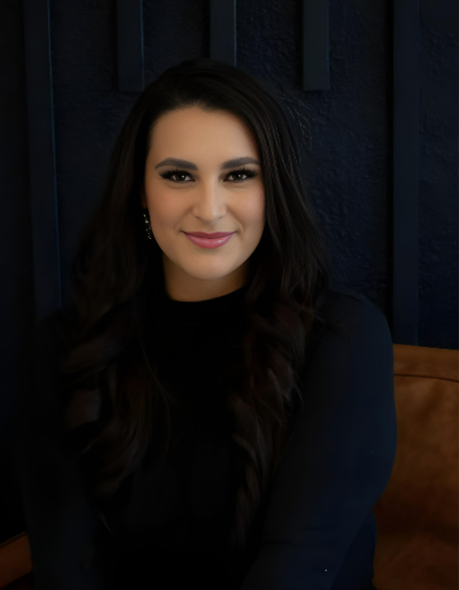 A woman in a black shirt is sitting on a couch and smiling for the camera.