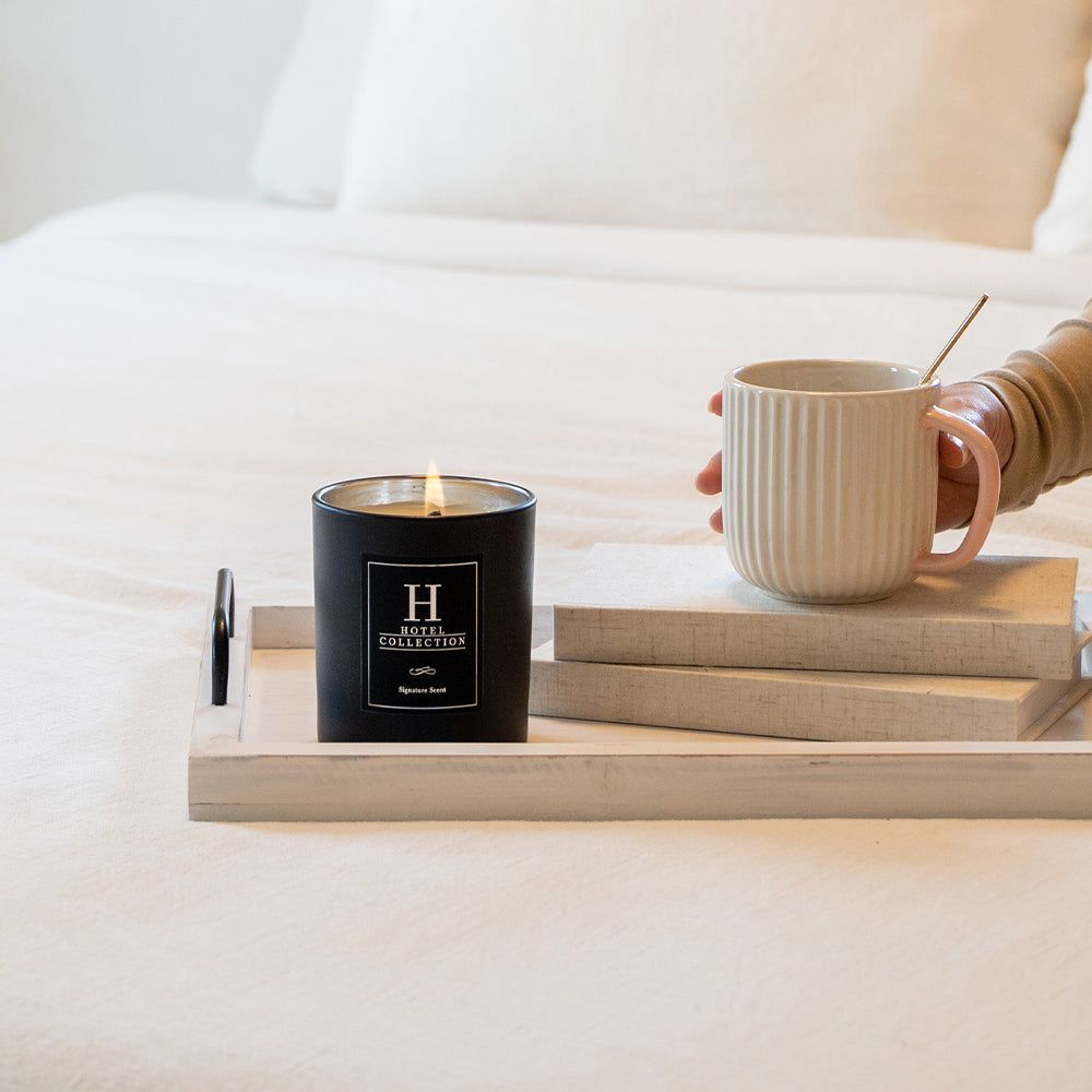 A person is holding a cup of coffee and a candle with the letter h on it