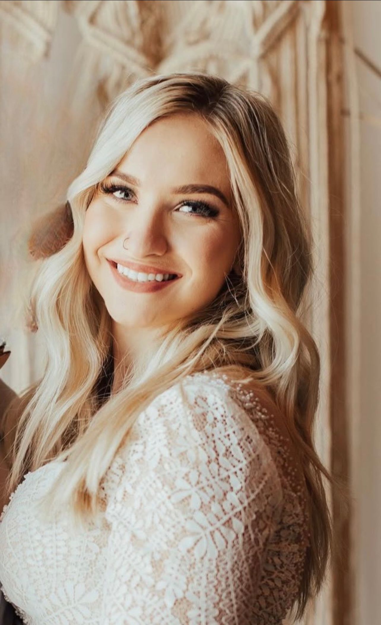 A woman in a white lace top is smiling and looking at the camera.