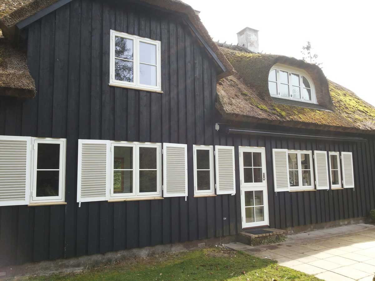Sort hus med hvidindrammede vinduer, skodder og stråtag.
