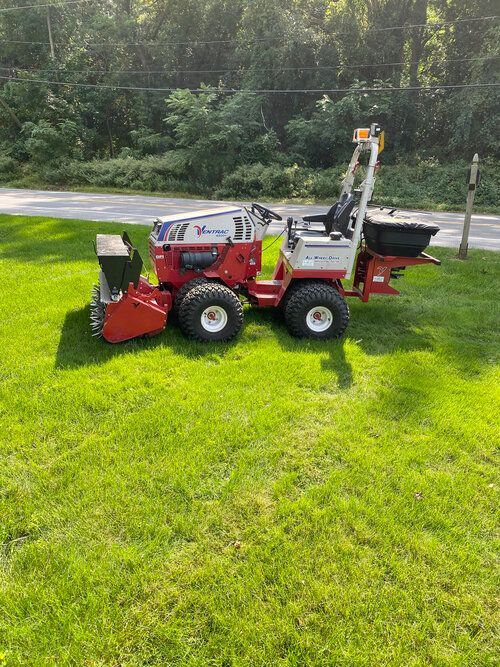 A lawn mower with a rake attached to it is sitting on top of a grassy hill.