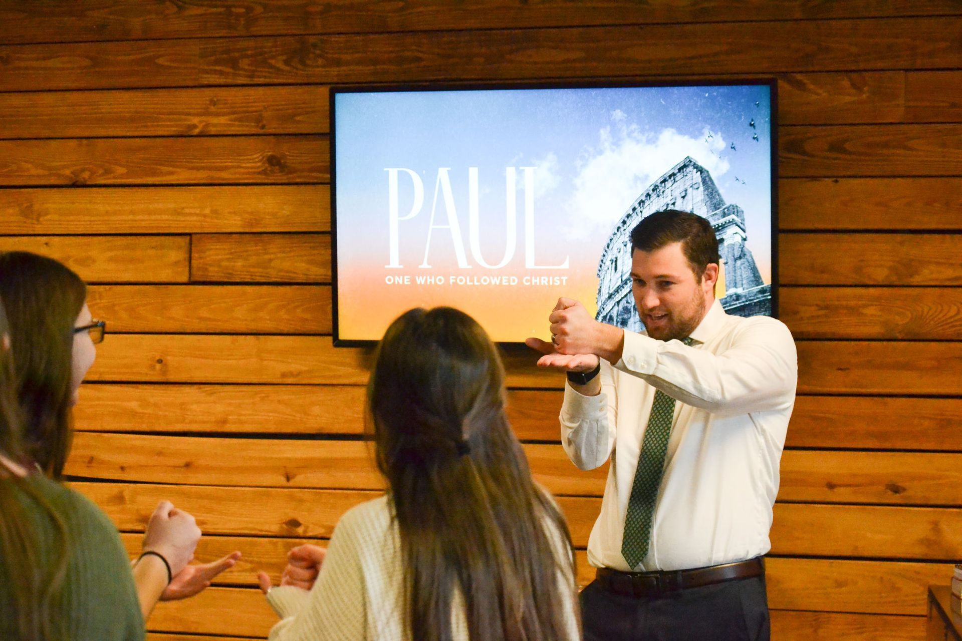 Man gesturing to two women in front of a screen; 