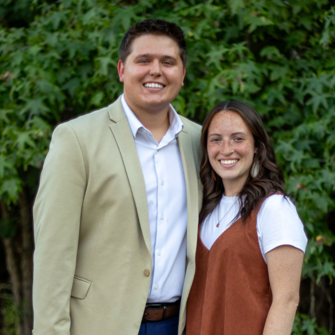 A couple stands in front of trees.