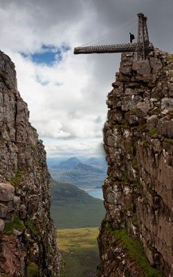 A person is standing on top of a rocky cliff with a bridge