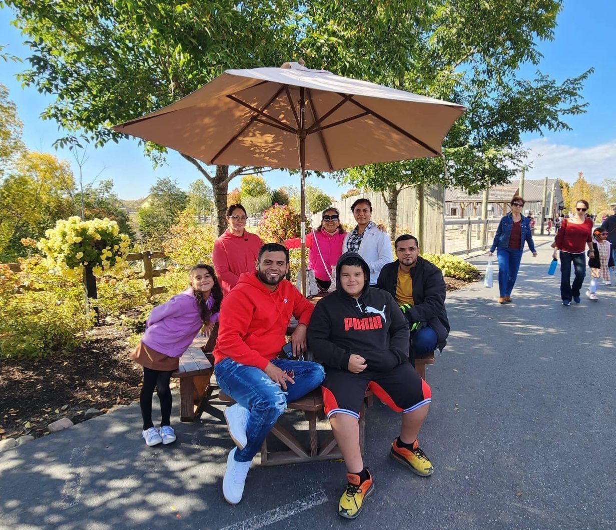 Family poses under an umbrella at an outdoor park on a sunny day.