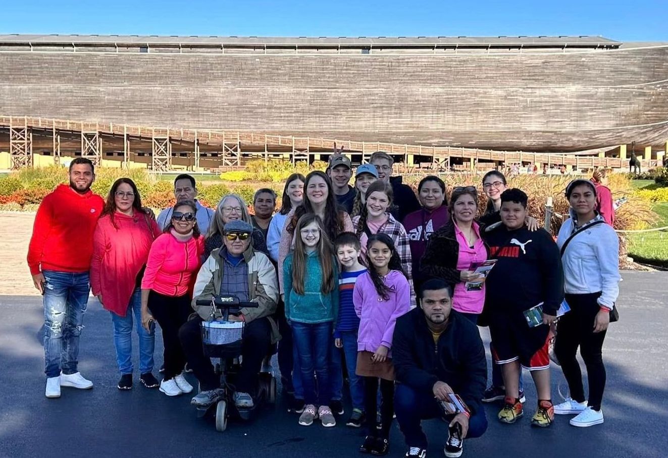 A group of people pose in front of a large wooden structure on a sunny day.
