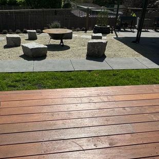 Outdoor patio with wooden deck, grass, stone stools, and a round table in a sunny courtyard.