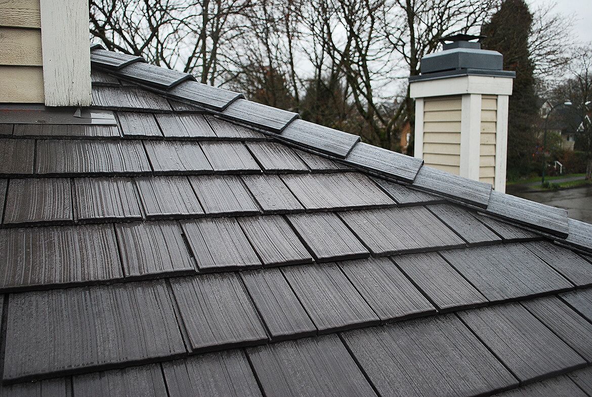 A close up of a roof with a chimney in the background.