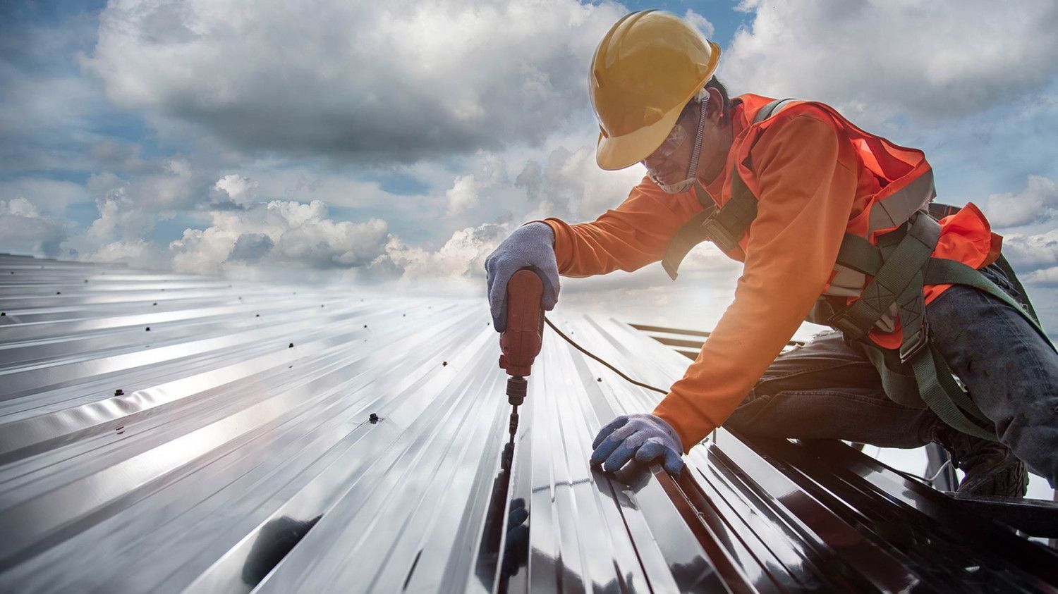 A construction worker is repairing a metal roof with a drill.