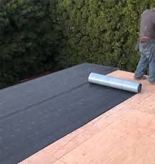 A man is laying a roll of roofing material on a wooden roof.