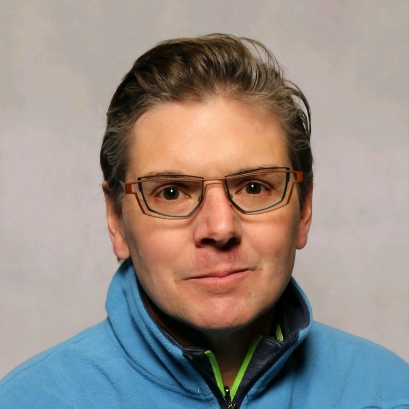 Woman with glasses atop her head, smiling slightly, in a black shirt.