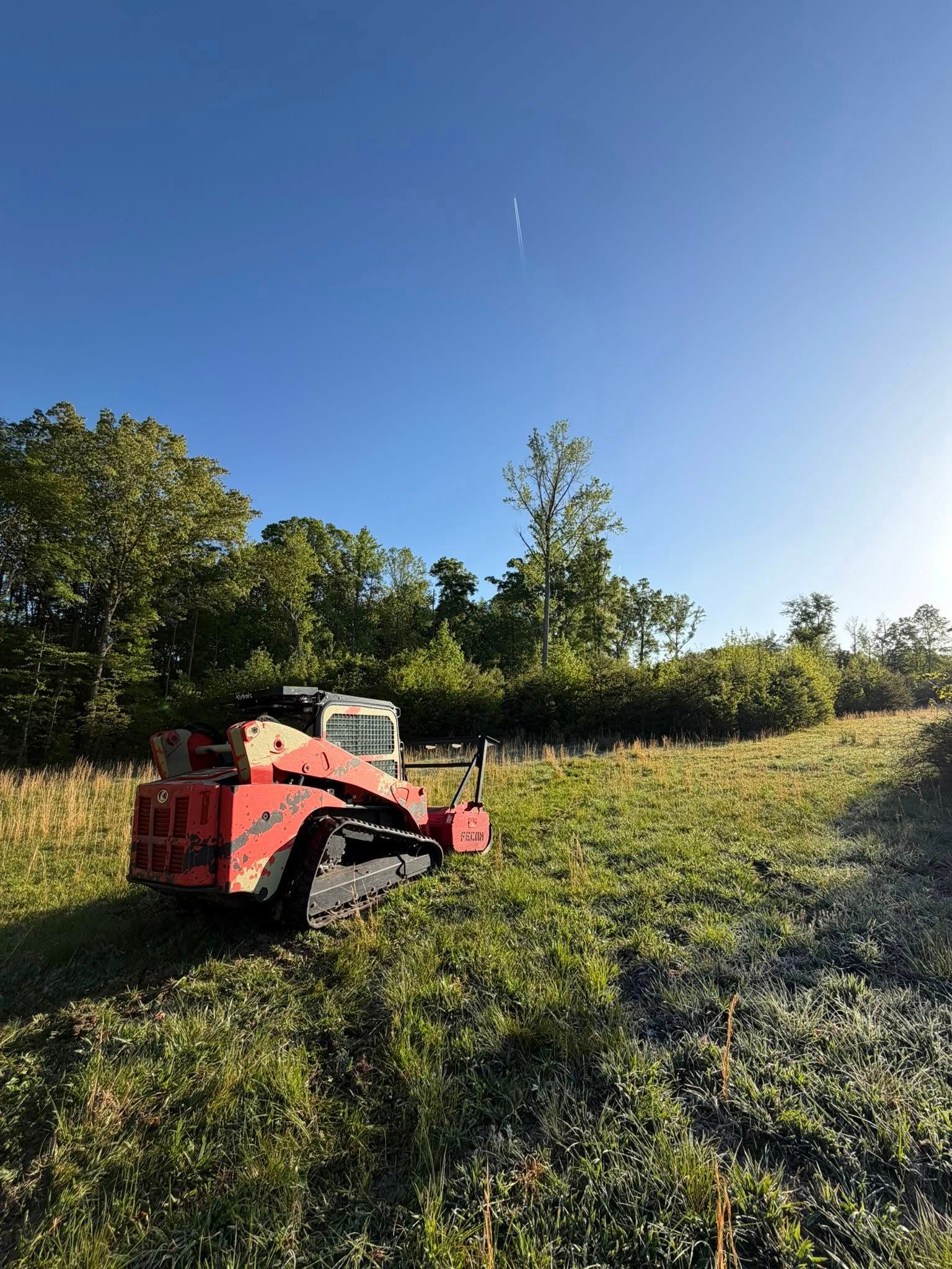 Red tractor mowing a grassy field under a clear blue sky.