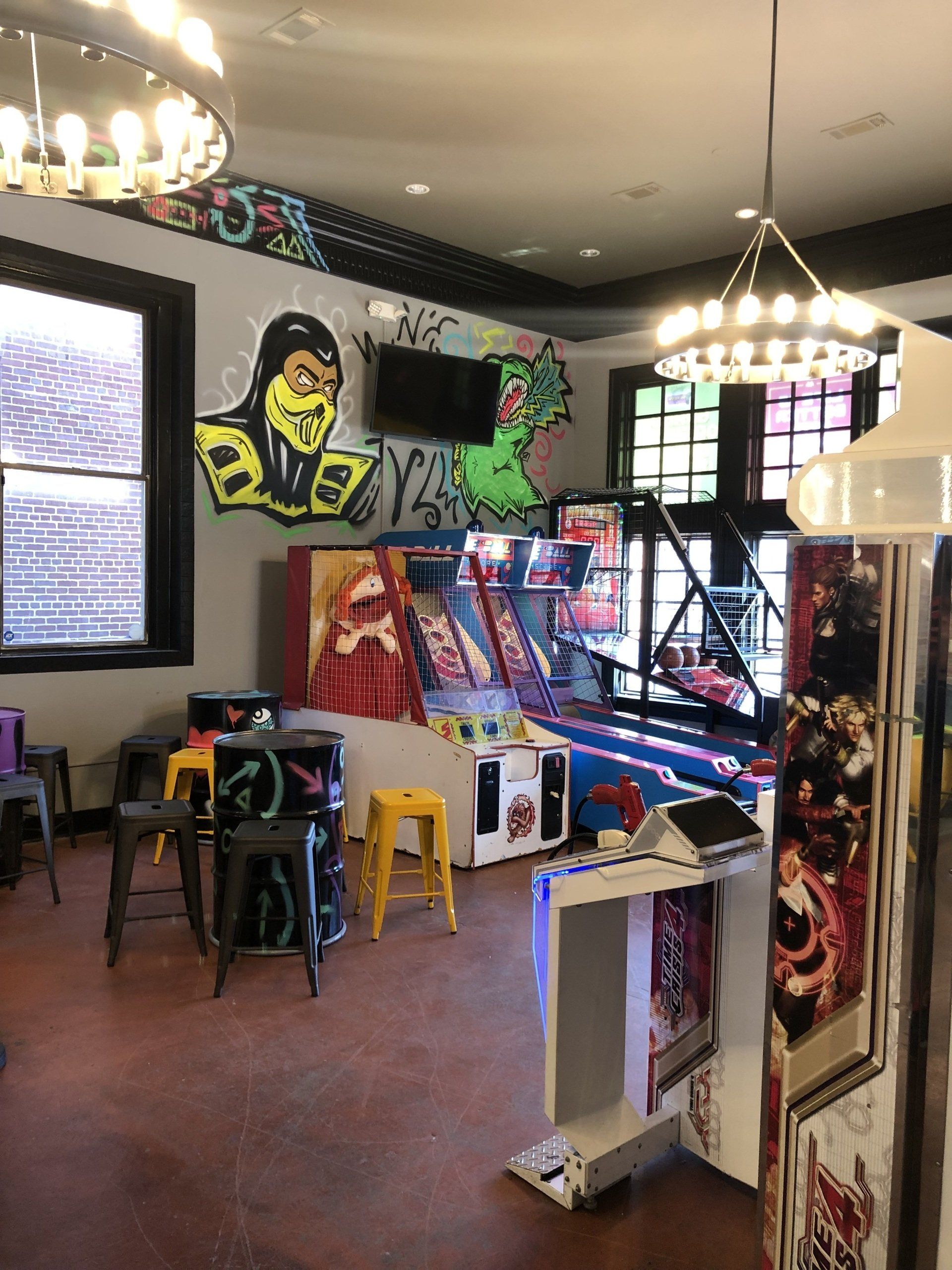 A room with a lot of arcade games and a mural on the wall.