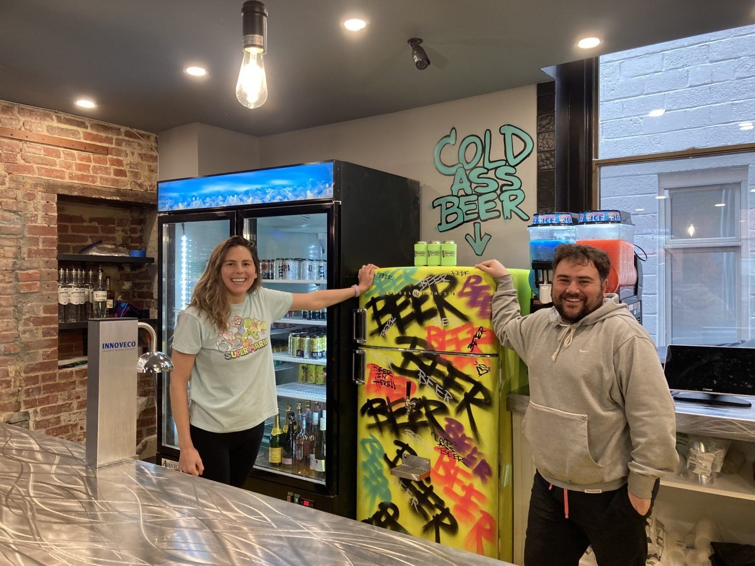 A man and a woman are standing next to a graffiti covered refrigerator.