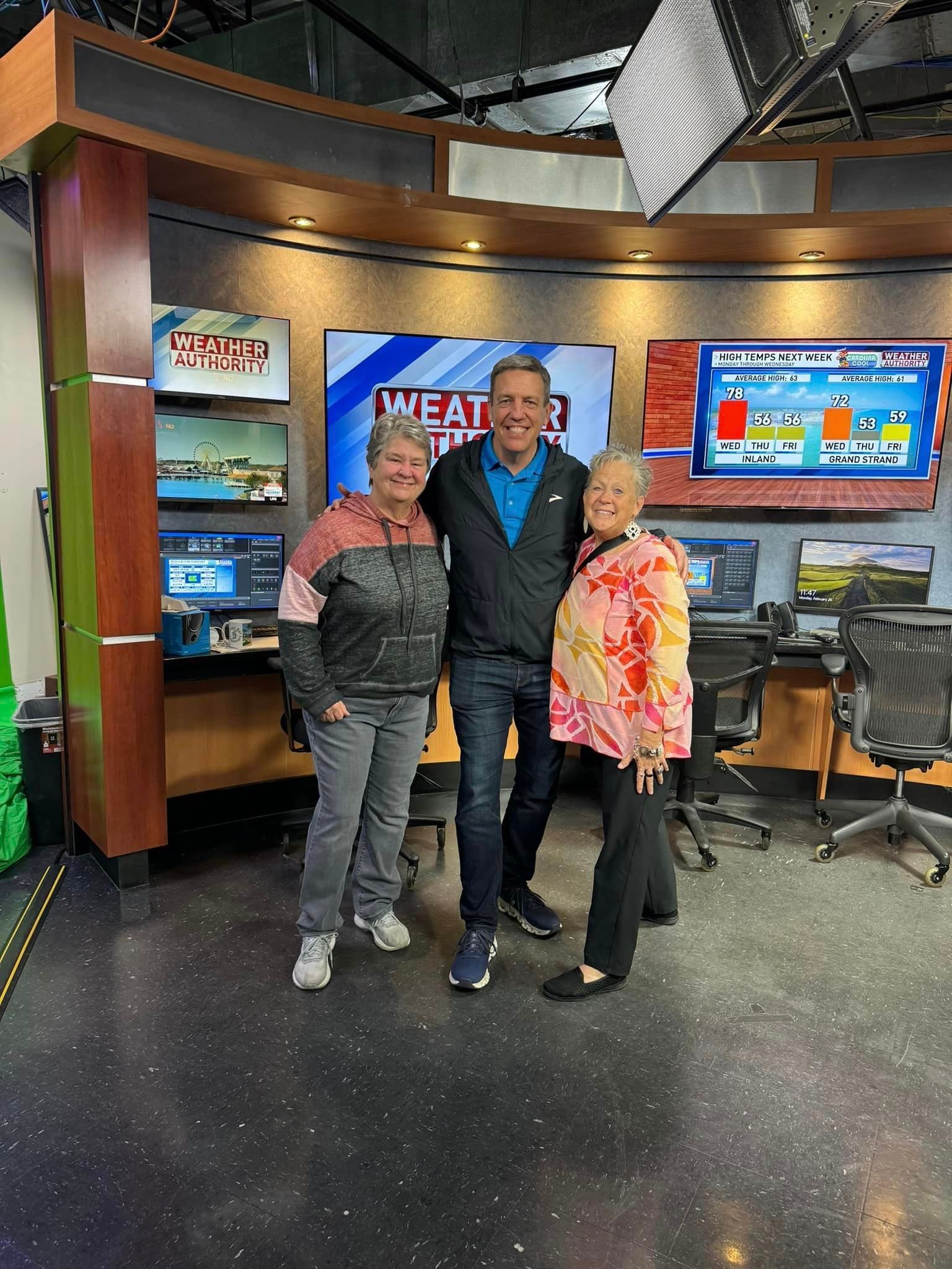 A man and two women are posing for a picture in a news studio.