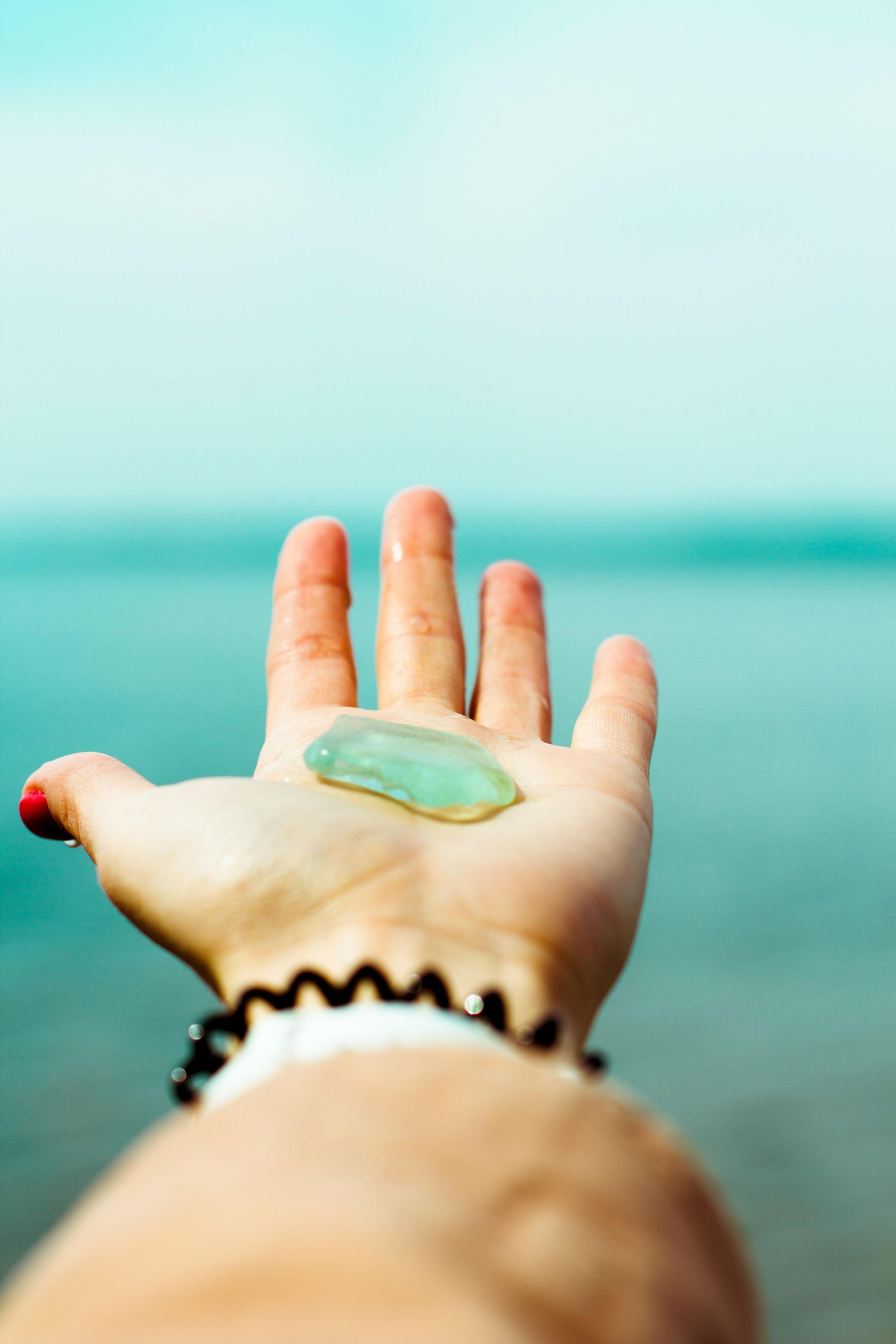 Hand holding a sea glass piece, with ocean and sky in background.