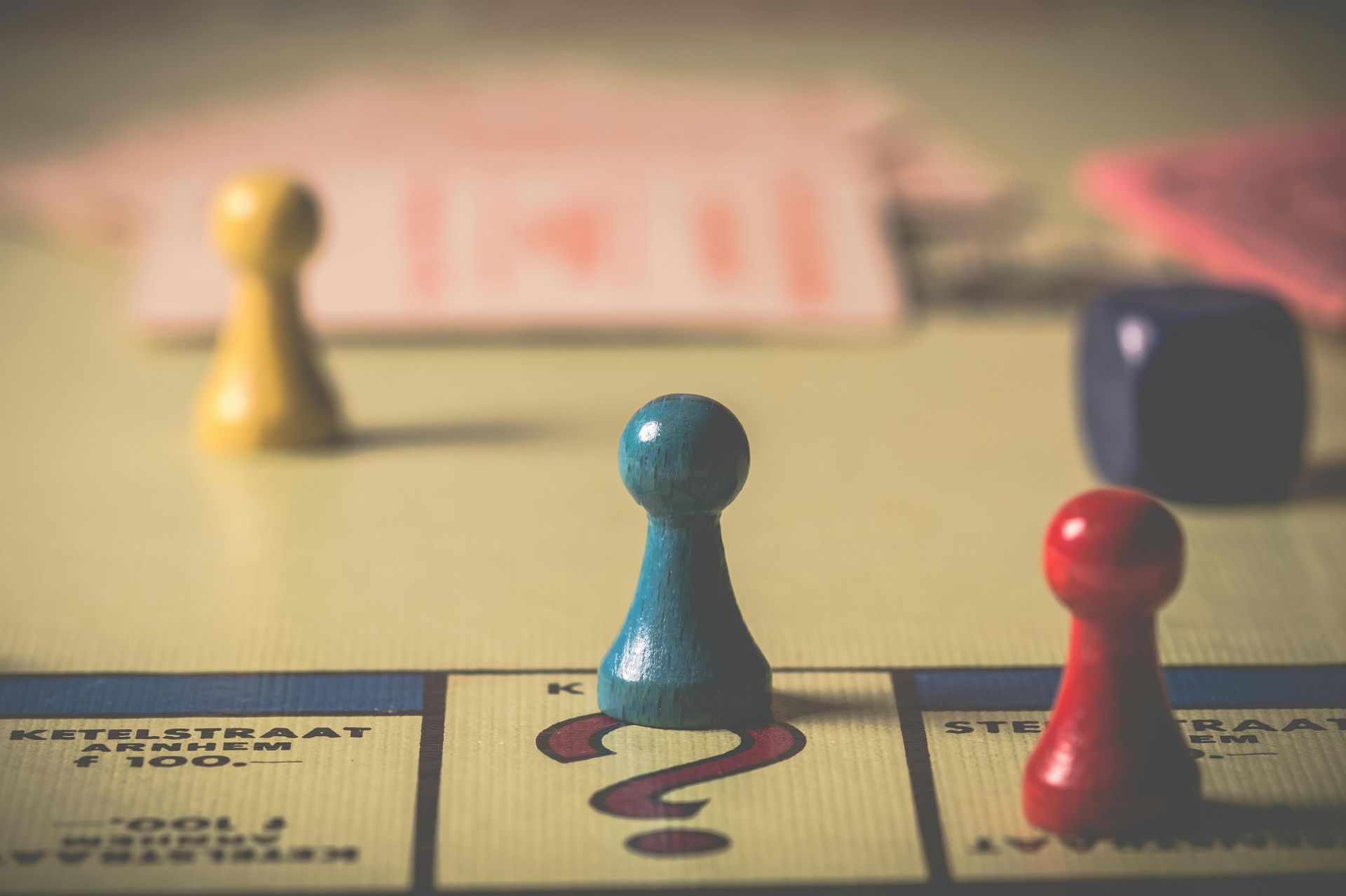 Monopoly board with blue, yellow, and red game pieces. Question mark space. Dice visible.