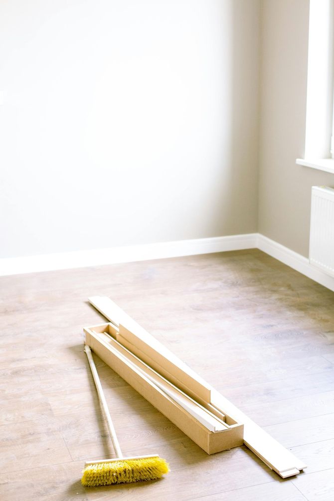 Empty room with light wood floor, beige walls, and window; broom and wood trim on floor.