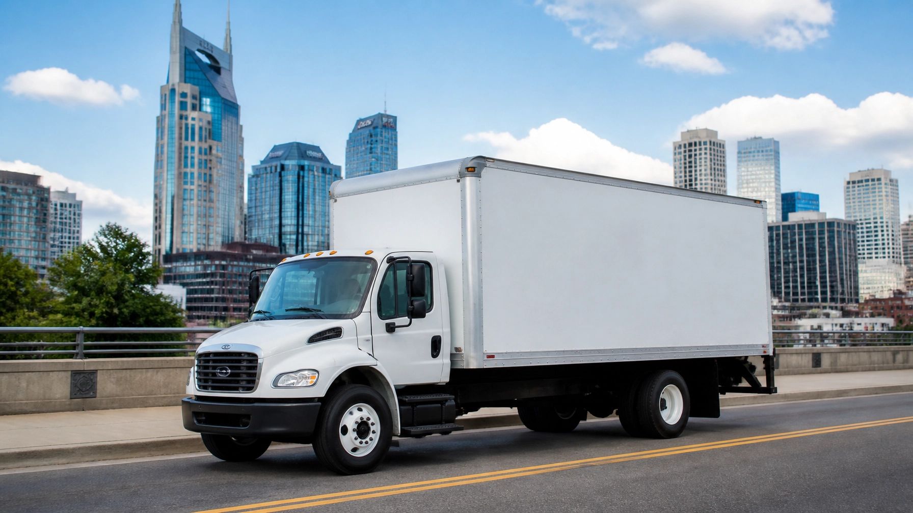 White box truck driving on a city bridge with a skyline in the background