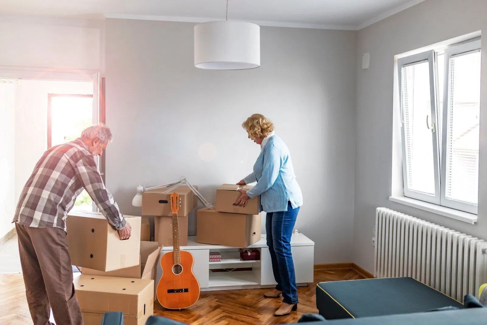 Two people unpacking boxes in a bright room with a guitar on the floor