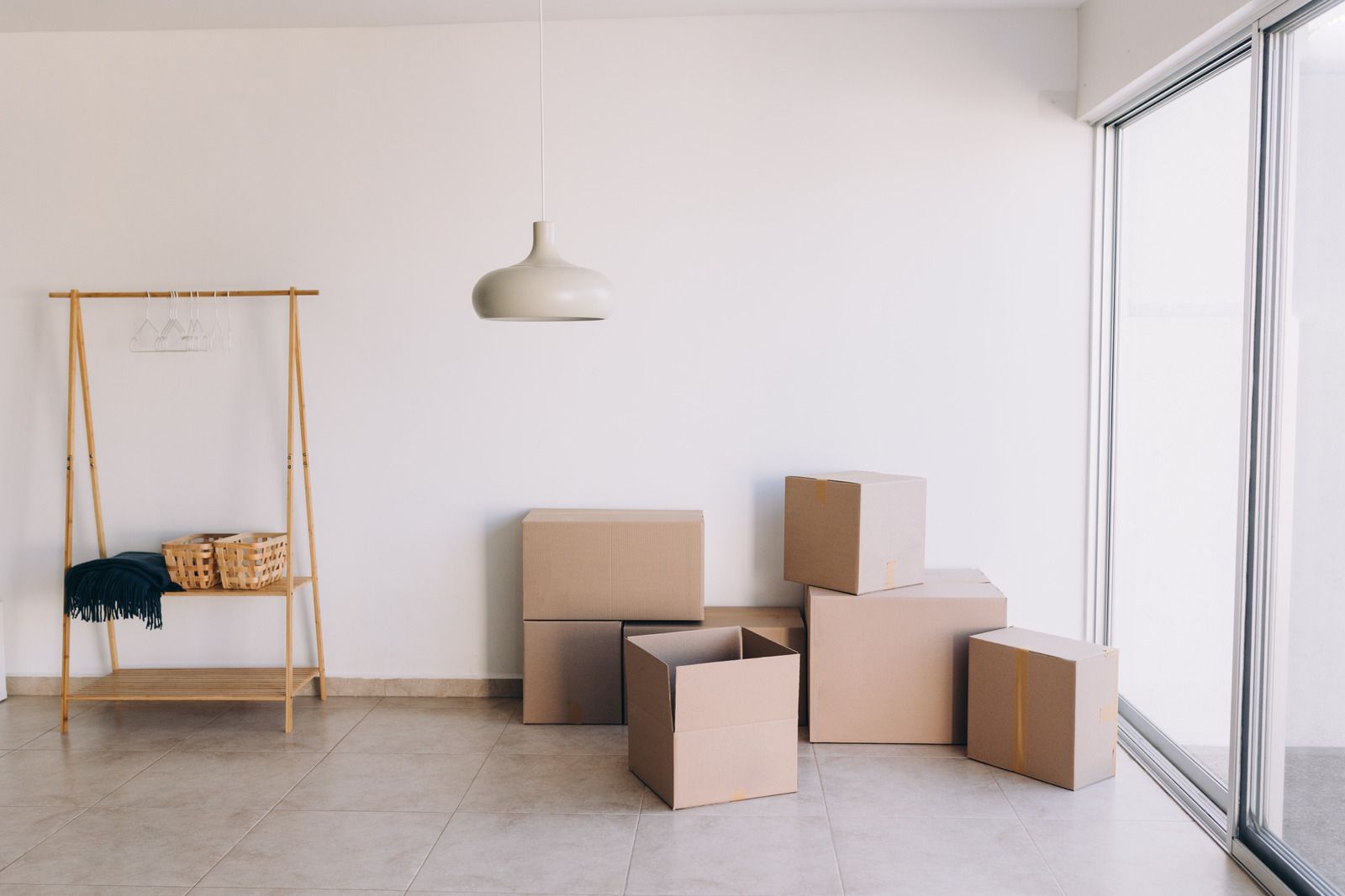 An empty room with cardboard boxes and a clothing rack. Light-colored walls and flooring