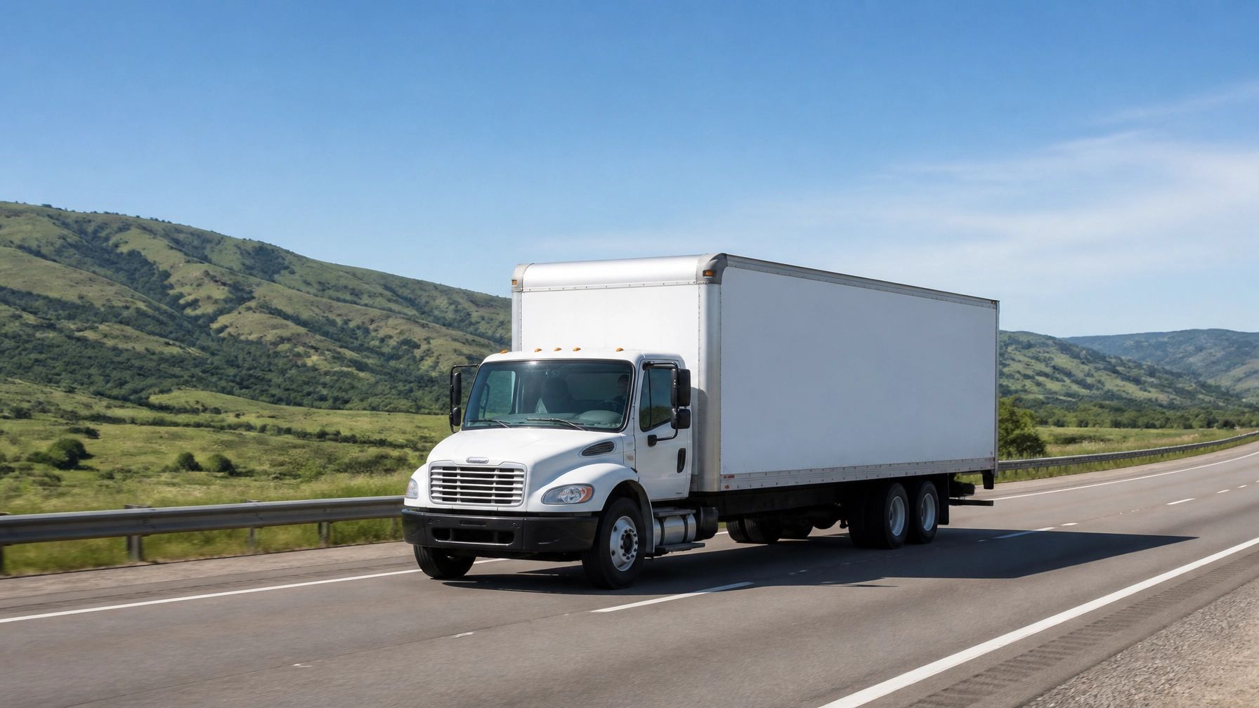 White box truck driving on a highway with green hills under a clear blue sky