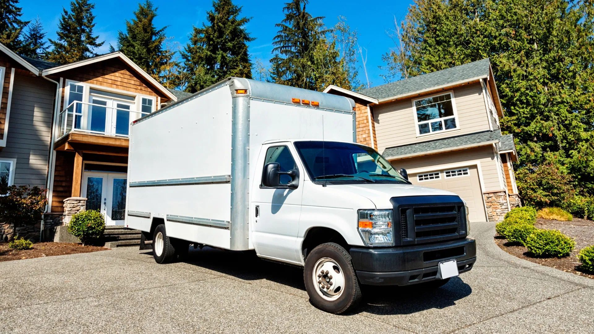 White box truck parked in a suburban driveway in front of a two-story house.
