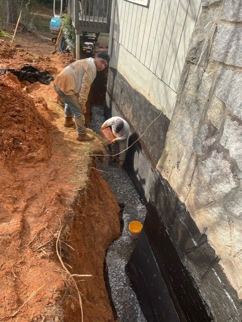 A man is digging a hole in the ground next to a house.