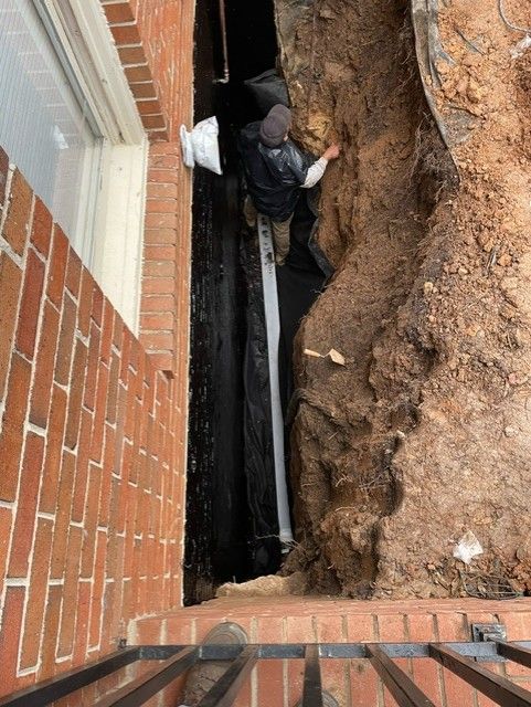 A man is digging in the dirt next to a brick wall