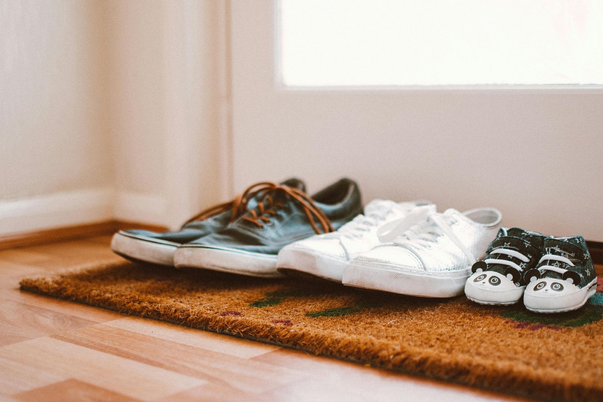 Shoes on a doormat inside a doorway: blue and white sneakers, and tiny baby shoes.