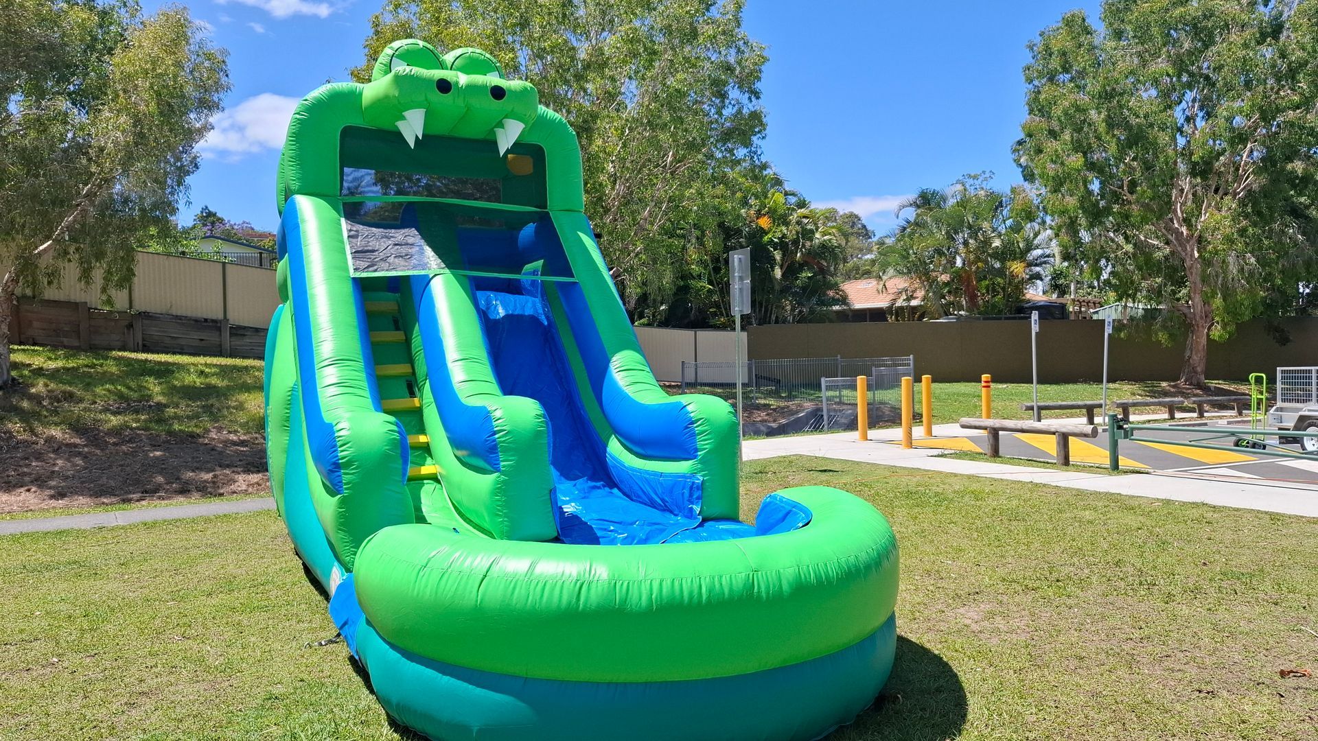 Green inflatable double water slide in a sunny park, with trees and grass around it. - Bowen Hire in Bowen, QLD