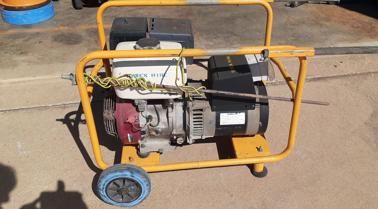 Portable generator in a yellow frame on pavement, with a white fuel tank and blue wheel. — Bowen Hire in Bowen, QLD