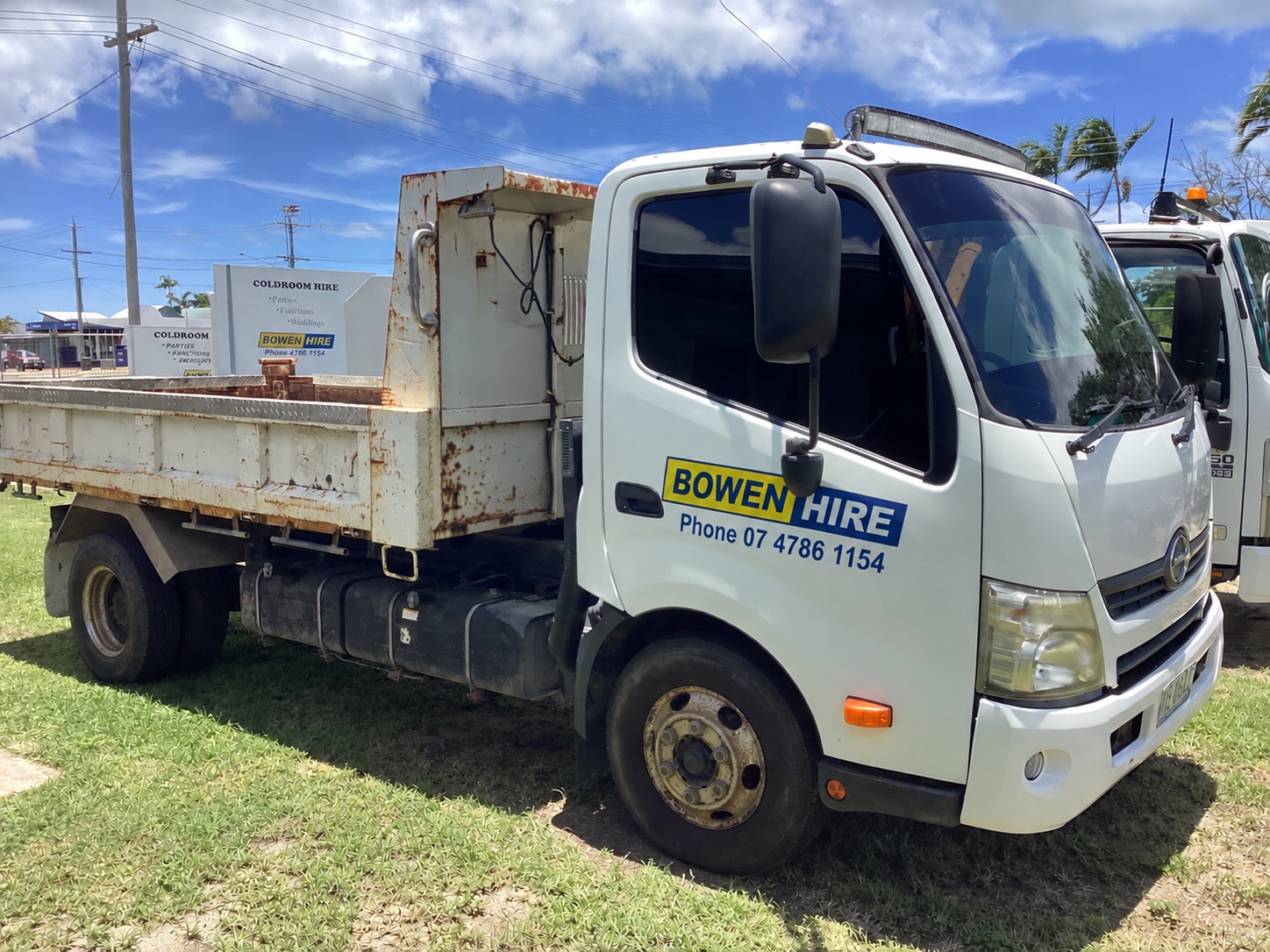 A White Dump Truck Parked on a Grassy Lot Under a Sunny Blue Sky — Bowen Hire in Bowen, QLD