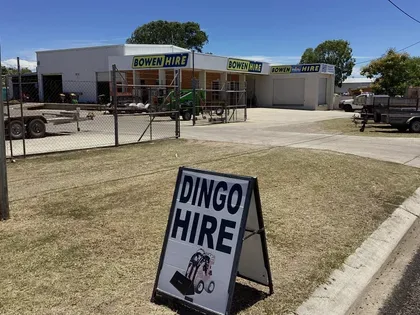 Dingo hire yard with equipment and a roadside sign in front under a clear blue sky — Bowen Hire in Bowen, QLD