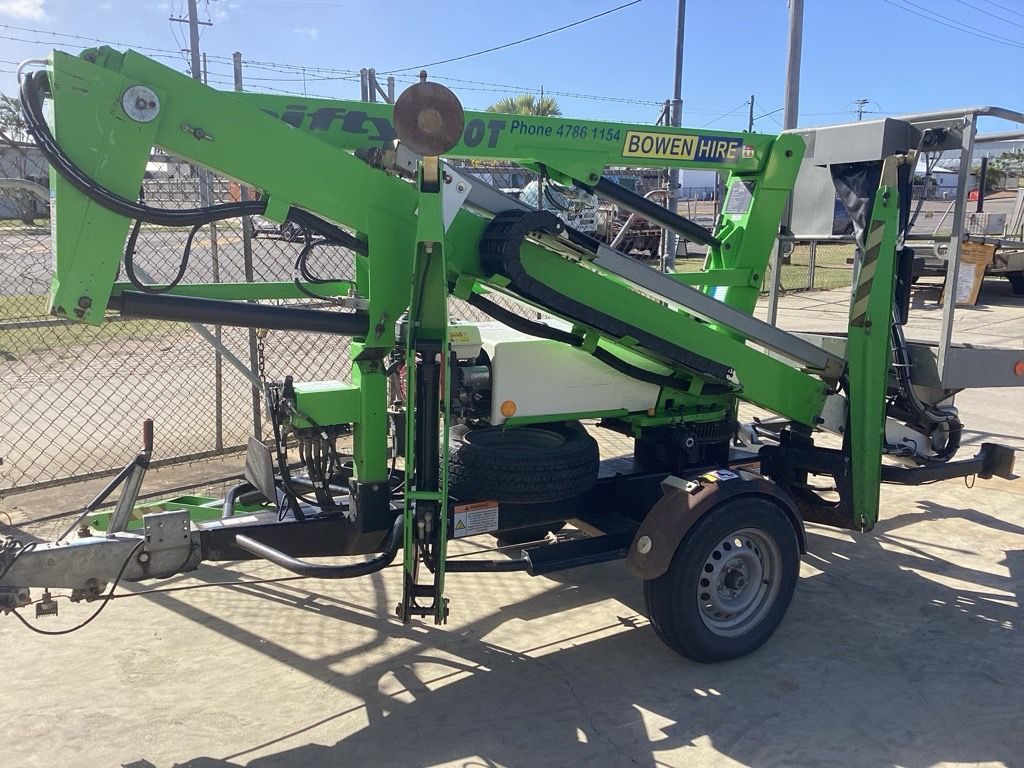 Green mobile hydraulic boom lift on a trailer at an outdoor worksite.