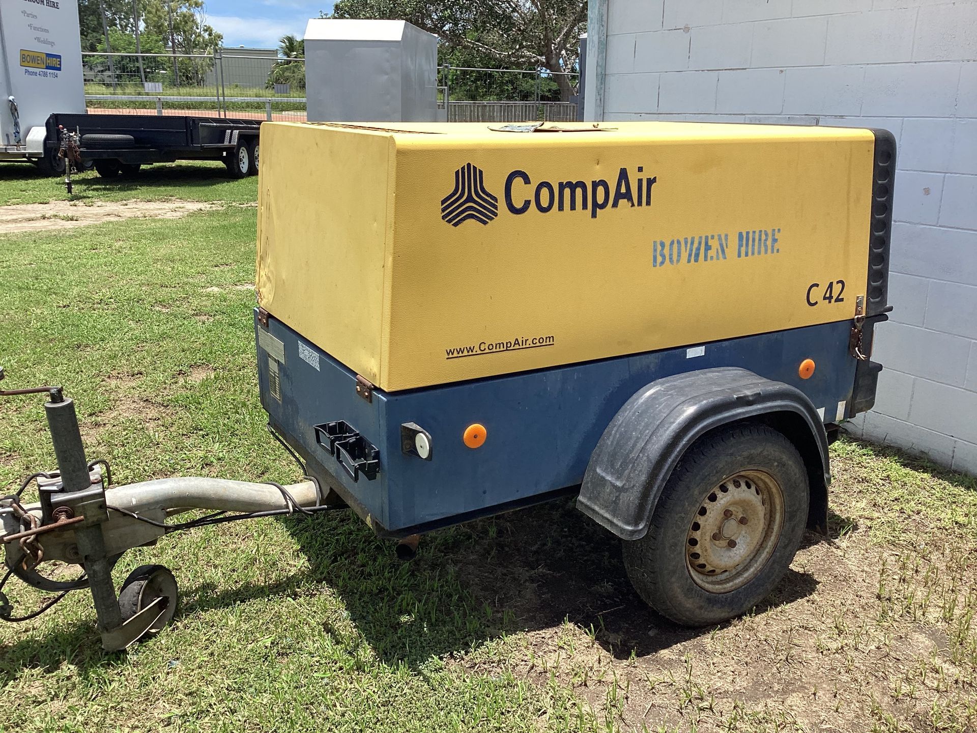 Yellow-and-blue Compair Towable Air Compressor Parked on Grass Beside a Building — Bowen Hire in Bowen, QLD