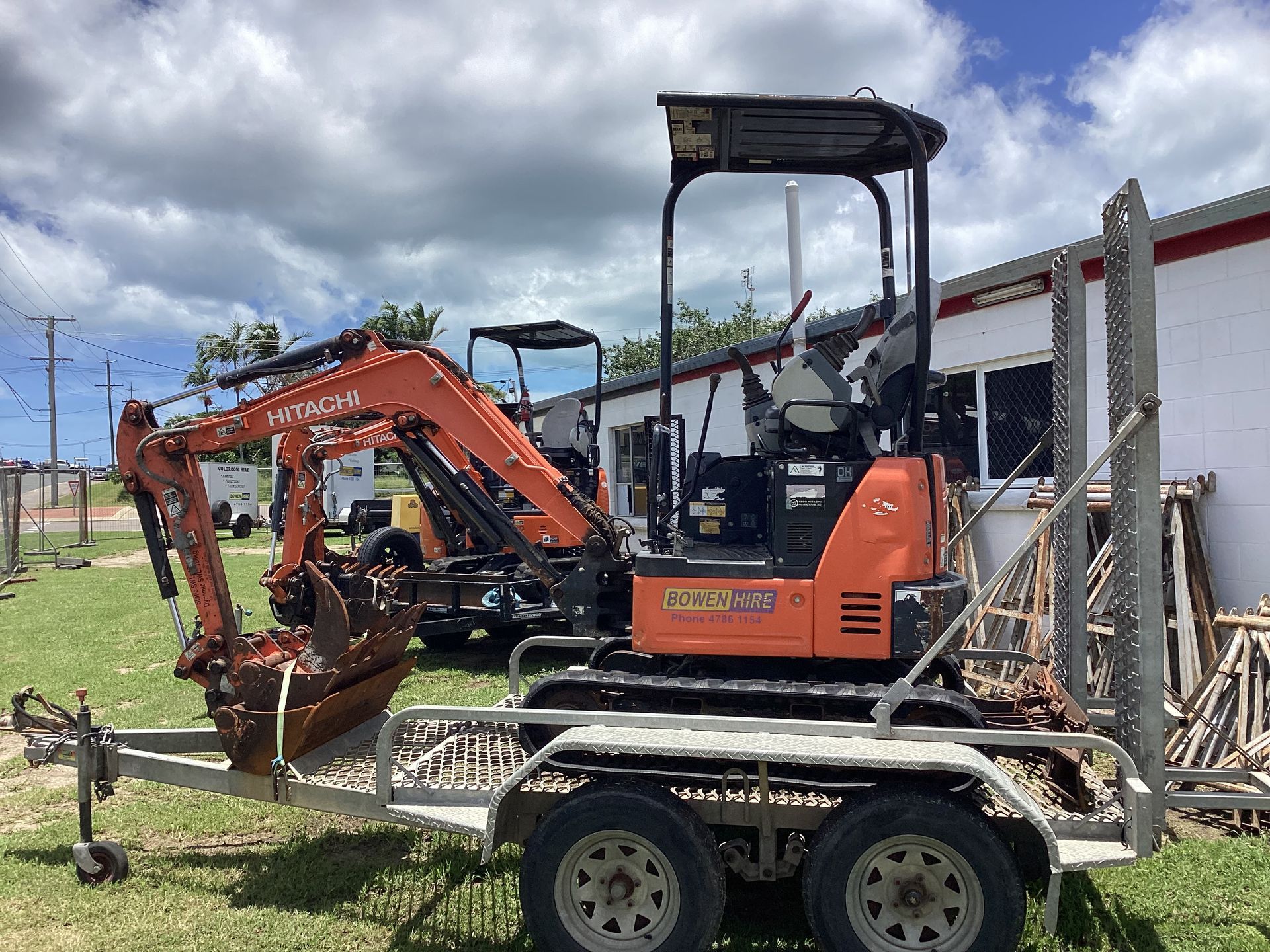 Orange Mini Excavator on a Trailer Beside a Fence Under a Cloudy Sky — Bowen Hire in Bowen, QLD