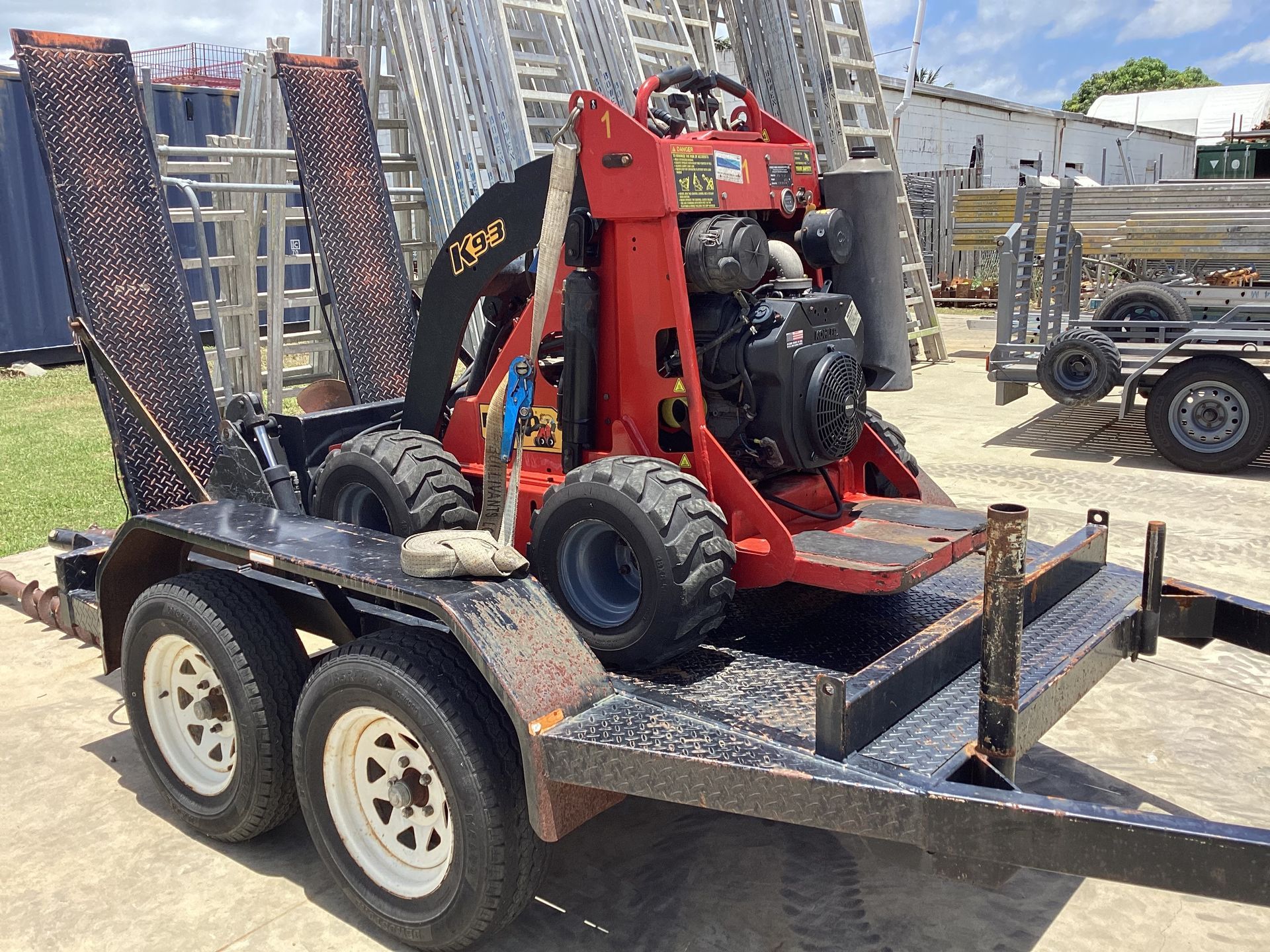Red Skid Steer Loader Strapped on A Black Trailer — Bowen Hire in Bowen, QLD